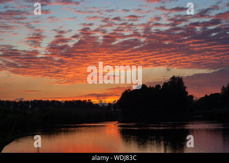 Altocumulus clouds over a lake are beautifully colored by the orange and purple light of the setting sun Stock Photo