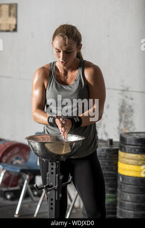 Female weight lifter preparing to lift by applying chalk to hands. Stock Photo