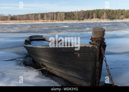 Winter scene of old wooden boat on ice of frozen lake. Stock Photo
