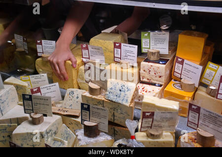 Madison, WI USA. Jul 2018. Assorted domestic and imported cheeses as an employee grabs a block to be cut and served to a waiting customer. Stock Photo