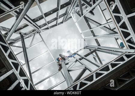 Steel Building Construction and Caucasian Contractor Worker at the Top of the Skeleton Steel Frame. Industrial Theme.