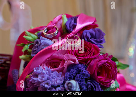colorful wedding bouquet with pink ribbon lying on the stone slabs . Engagement rings and ribbon on engagement red and purple bouquet . Stock Photo