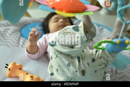 Baby girl plays with toys of activity gym on playmat Stock Photo