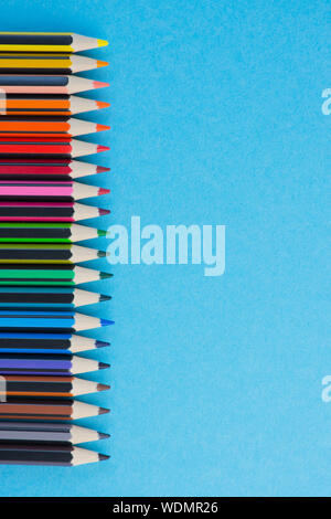 vertical photo of a row of colored pencils with different colors against light blue background, pencils on the left side with copy space Stock Photo