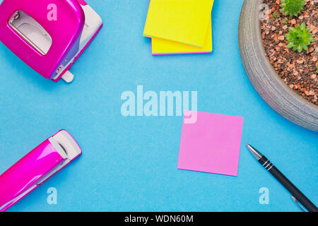 pink notepad with a pen on blue background beside pink punch and stapler, copy space Stock Photo