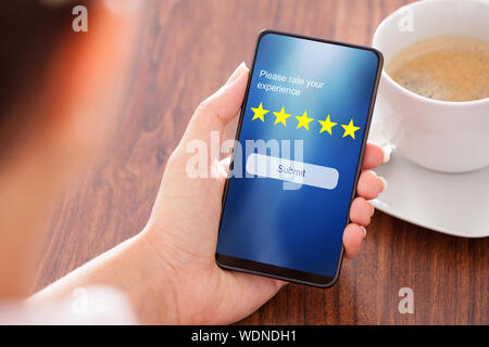 Businesswoman Using Mobile Phone In Restaurant To Send Rating With Online Website Over The Wooden Stock Photo