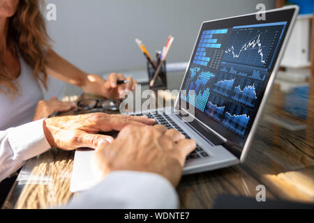 Close- Up Of Office Workers Analyzing Graph On Laptop With His Coworker Stock Photo