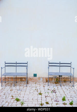 Empty Metallic Chairs On Footpath Against White Wall