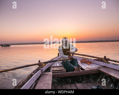 Indian man rowing a boat down the Ganges River at down in Varanasi, Uttar Pradesh, India, Asia Stock Photo