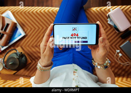 modern woman sitting on divan in the modern living room having 404 page not found error on a smartphone. Stock Photo