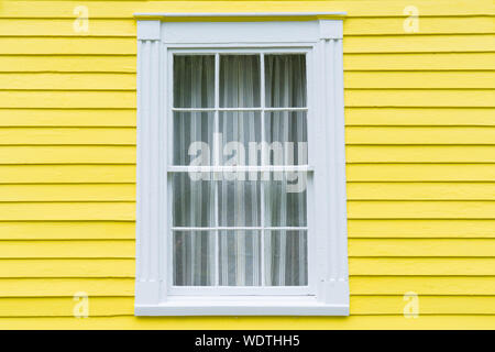 Old wood frame window with bright yellow clapboard siding Stock Photo