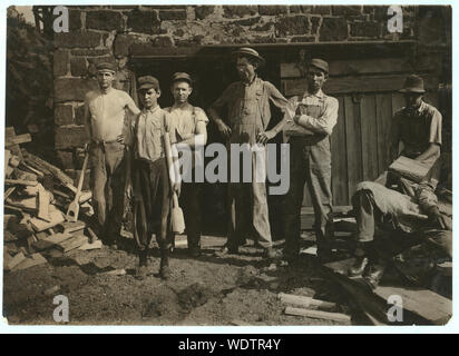 Group outside Pittman Handle Factory. A fifteen year old boy operating a dangerous boring machine at which he said a boy recently bored half his hand off. To operate this machine (which bores a large hole in the spade handle) the boy has to throw his whole weight onto the lever which pushes the handle (and himself) up against the unprotected borer. A slip might easily result fatally. Boy earns $1.65 a day. This factory has a number of unprotected belts and dangerous machines. One other boy, about the age of this one, was doing all kind[s] of work, taking away the handles from a huge rip saw, e Stock Photo