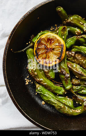 Sesame blistered shishito peppers with lemon, sesame oil and sesame seeds cooked in a cast-iron pan (Capsicum annuum var) Stock Photo