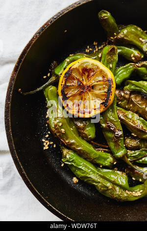 Sesame blistered shishito peppers with lemon, sesame oil and sesame seeds cooked in a cast-iron pan (Capsicum annuum var) Stock Photo