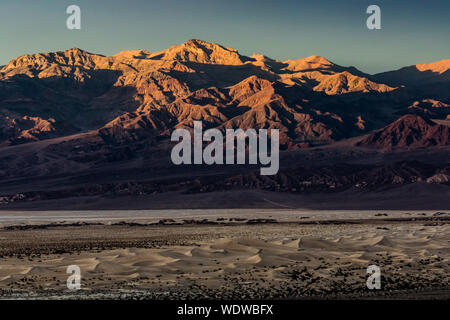 Sunset illuminating Thimble Peak in Death Valley National Park with Mesquite Sand Dunes in the foreground Stock Photo