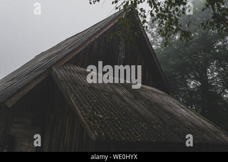 Very old rural barn during early morning fog in autumn. In the background visible birch tree and forest. Very mysterious and frightening atmosphere Stock Photo