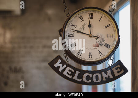 Vintage clock with roman number and welcome label hanging on ceiling Stock Photo