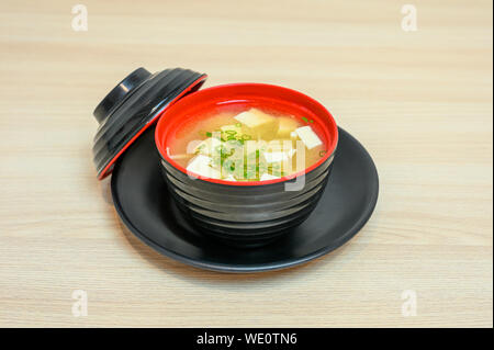 Miso soup with tofu and vegetable in black cup with lid on wooden table Stock Photo