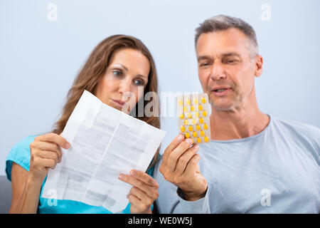 Matured Couple Sitting On Sofa Reading A Leaflet After Taking Pills At Home Stock Photo
