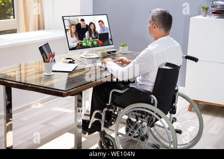 Handicapped Businessman Sitting On Wheelchair And Using Computer In Office Stock Photo