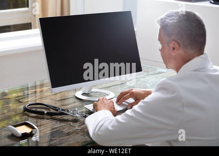 Confident Male Doctor Working On Computer At Desk Stock Photo
