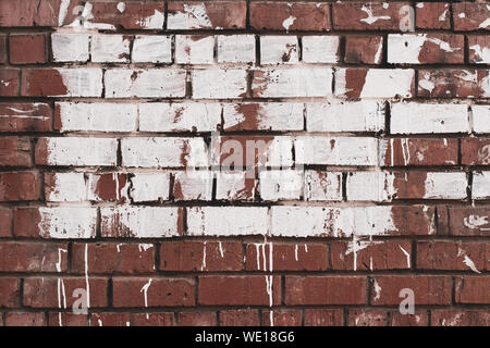 Abstract grunge background. Old brick wall stained with paint. White paint with smudges on red brick. Stock Photo