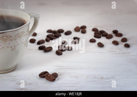 A cup of coffee with steam on a white background in paint and coffee beans are nearby. Selective focus on the first coffee beans, others blurred. Plac Stock Photo