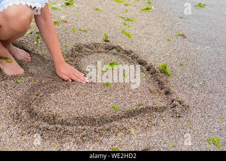 Young woman drawing a heart in the wet sand at the seaside Stock Photo