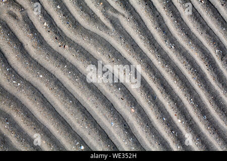 Silver gray sand on sea beach top view close up, ribbed dry sand surface pattern, wavy curved diagonal lines texture, abstract curves background Stock Photo
