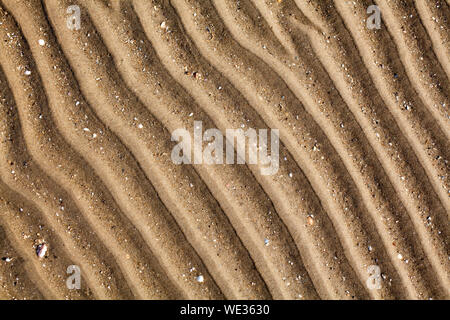 Yellow golden sand on sea beach top view close up, ribbed dry sand surface pattern, wavy curved diagonal lines texture, abstract curves background Stock Photo