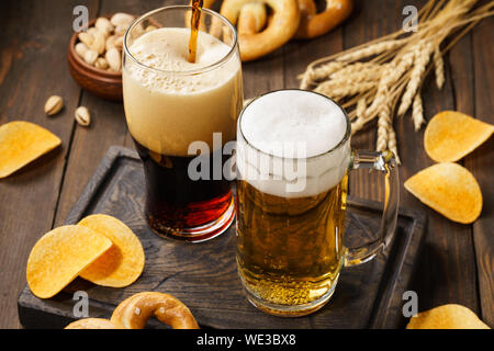 Light and dark beer with various snacks - chips, pretzels and nuts on a dark wooden background. Stock Photo