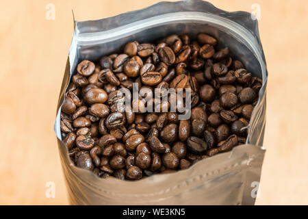Coffee beans in a plastic foil package on wooden background. Roasted aromatic coffee top view. Stock Photo