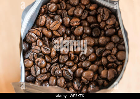 Coffee beans in a plastic foil package on wooden background. Roasted aromatic coffee top view. Stock Photo