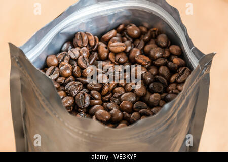 Coffee beans in a plastic foil package on wooden background. Roasted aromatic coffee top view. Stock Photo