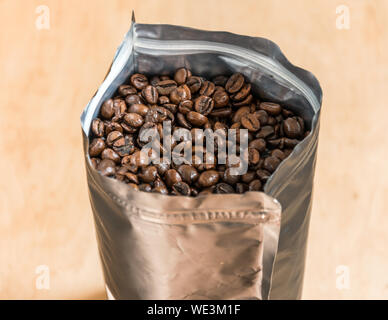 Coffee beans in a plastic foil package on wooden background. Roasted aromatic coffee top view. Stock Photo