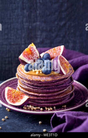 Healthy lilac pancakes with chokeberry and acai powder topped with peanut butter with figs and blueberries Stock Photo