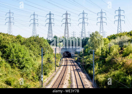 The LGV Atlantique high-speed railway passing in a tunnel under a row of electricity pylons in the suburbs of Paris, France, on a sunny summer day. Stock Photo