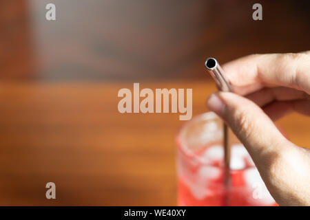 hand holding metal straw in a glass of red sweet drink Stock Photo
