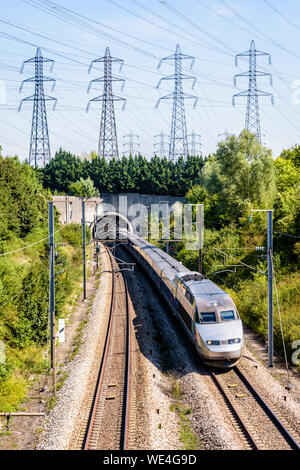 A TGV high-speed train in Atlantic livery is coming out of a tunnel under a row of transmission towers on the LGV Atlantique high-speed railway.
