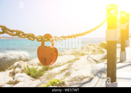Red love padlock attached to chain. Rusty lock with heart shape carved hanging outdoors. Valentines day, unity, memory concepts. Stock Photo