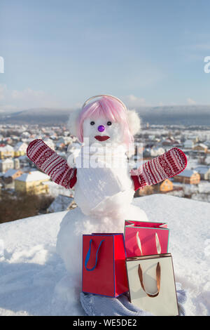 Snowman in pink wig and mittens with gift pack. Stock Photo