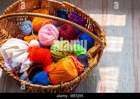 Wooden basket with rainbow natural balls of yarn on an old traditional carpet. Symbols of knitting and a tractional female hobby Stock Photo