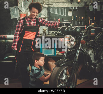 African american woman mechanic and boy helper repairing a motorcycle in a workshop Stock Photo