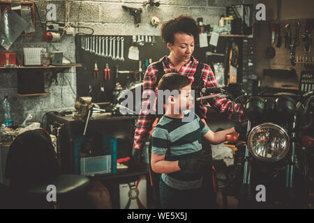 African american woman mechanic and boy helper repairing a motorcycle in a workshop Stock Photo