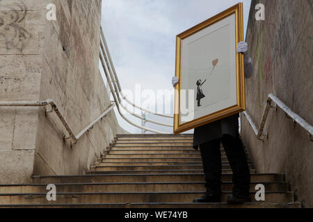 London, UK. 30th Aug, 2019. A Christie's employee poses with artworks 'Girl with balloon - Colour AP (Gold)' by anonymous street artist Banksy at the Southbank Centre in London Friday, August 30, 2019. The Southbank Centre was near one of the original locations the artwork appeared in London. The screen prints will be on sale during an online only auction titled 'Banksy : I can't believe you morons buy this sh*t' presented by Christie's auction house between 11-24 September 2019. Photograph Credit: Luke MacGregor/Alamy Live News Stock Photo