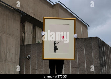 London, UK. 30th Aug, 2019. A Christie's employee poses with artworks 'Girl with balloon' by anonymous street artist Banksy at the Southbank Centre in London Friday, August 30, 2019. The Southbank Centre was near one of the original locations the artwork appeared in London. The screen prints will be on sale during an online only auction titled 'Banksy : I can't believe you morons buy this sh*t' presented by Christie's auction house between 11-24 September 2019. Photograph Credit: Luke MacGregor/Alamy Live News Stock Photo