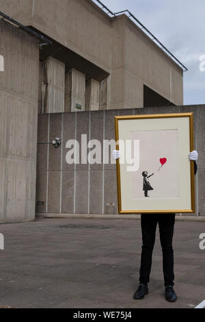 London, UK. 30th Aug, 2019. A Christie's employee poses with artworks 'Girl with balloon' by anonymous street artist Banksy at the Southbank Centre in London Friday, August 30, 2019. The Southbank Centre was near one of the original locations the artwork appeared in London. The screen prints will be on sale during an online only auction titled 'Banksy : I can't believe you morons buy this sh*t' presented by Christie's auction house between 11-24 September 2019. Photograph Credit: Luke MacGregor/Alamy Live News Stock Photo