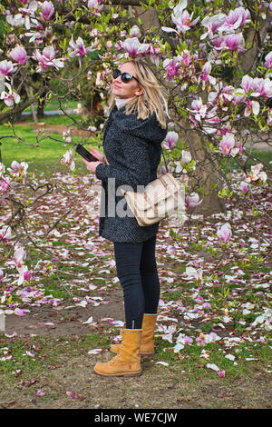 Portrait of the young woman standing in the park under magnolia tree Stock Photo