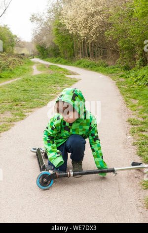 A young boy picking up a scooter outside Stock Photo