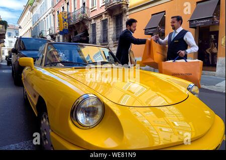 Italy, Lombardy, Milan, Fashion Quadrilateral (Quadrilatero della moda), Alfa Romeo Duetto Spider yellow cabriolet in front of the Four Seasons Hotel Milano, the doorman brings a Vuitton bag Stock Photo